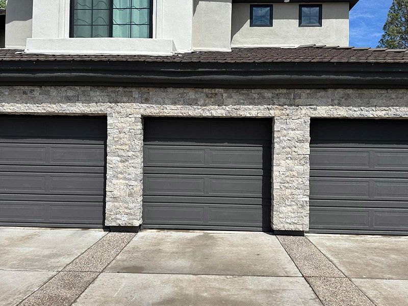 Three gray garage doors with stone accents on a concrete driveway.