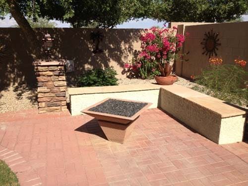 Patio with fire pit, stone benches, and flowering plants against a wall.