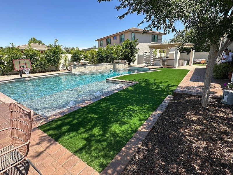 Backyard with pool, artificial turf, and outdoor kitchen on a sunny day.