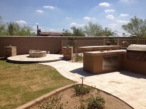 Backyard with a fire pit, outdoor kitchen, and landscaping under a sunny sky.