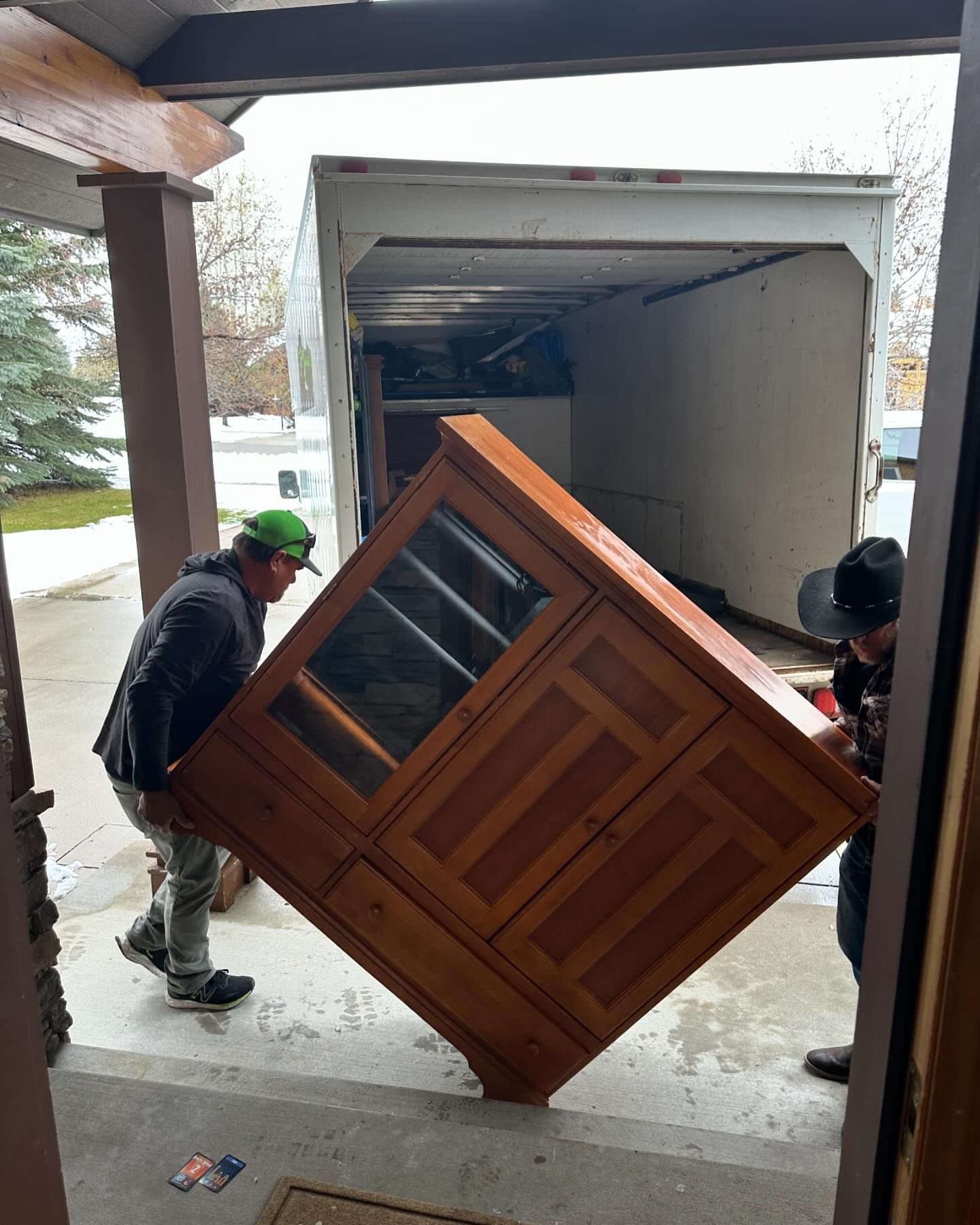 Two men are carrying a large wooden cabinet into a truck