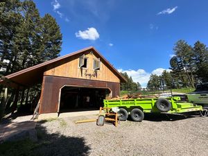 A green trailer is parked in front of a wooden garage.