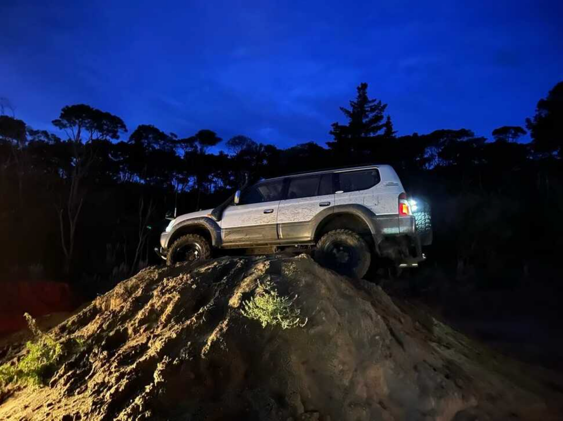 A white suv is driving down a dirt hill at night.