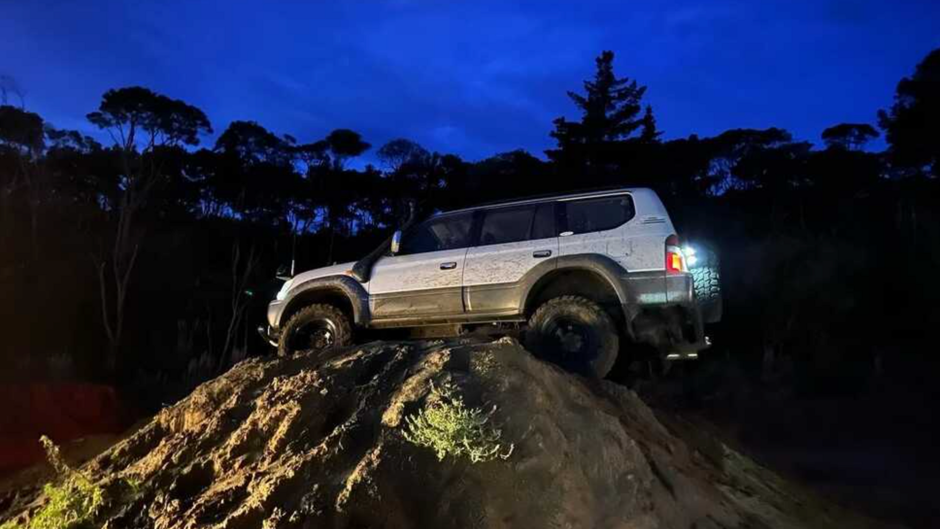 A white suv is driving down a dirt hill at night.