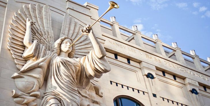 A statue of an angel holding a trumpet on the side of the bass hall building