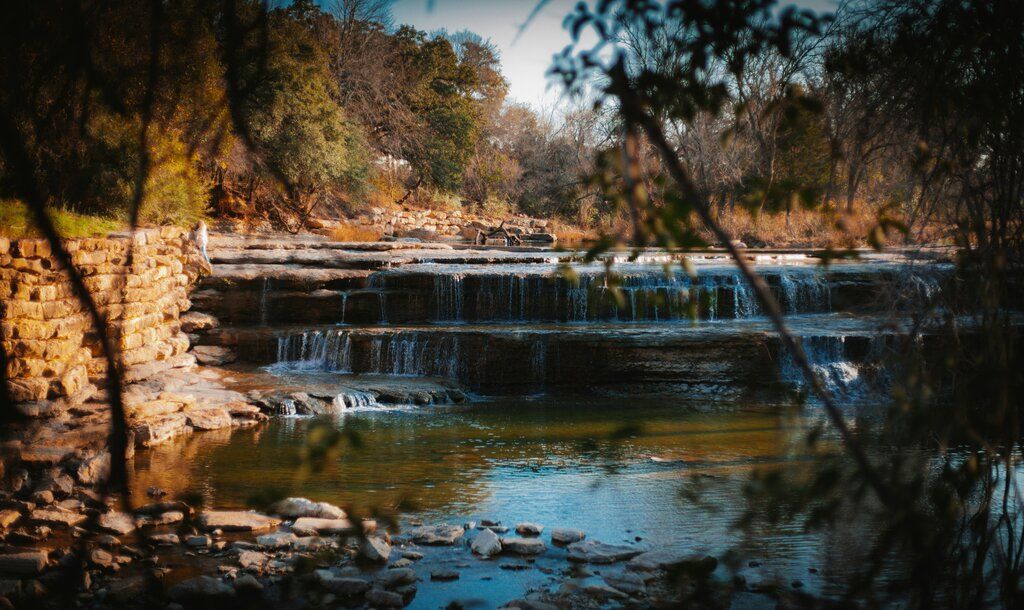 A waterfall is surrounded by trees and rocks in the middle of the trinity river.