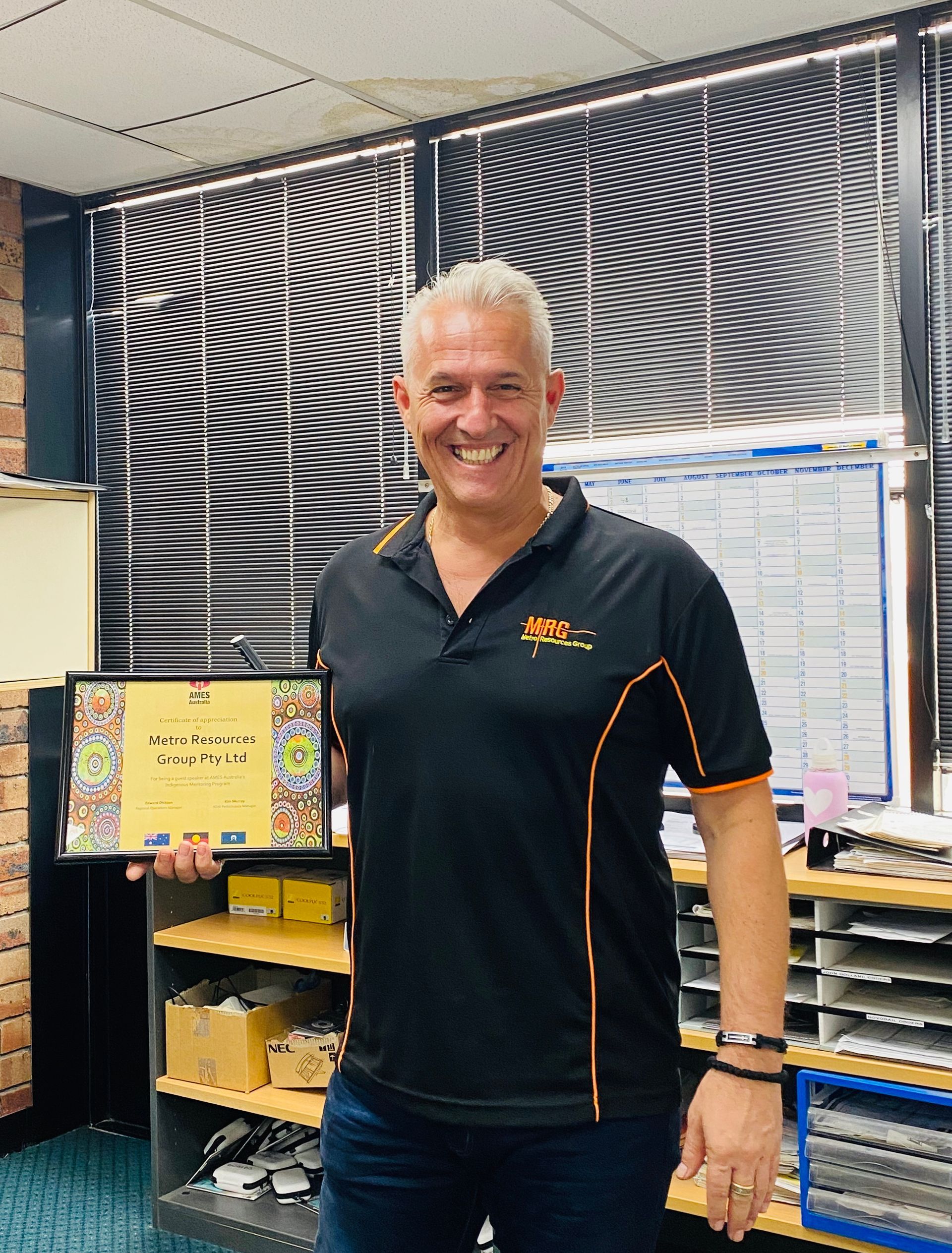 A man in a black shirt is holding a certificate in front of a window.
