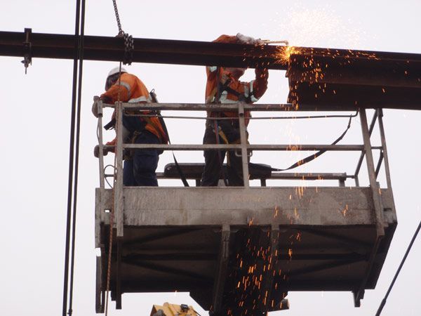 Two men are cutting a metal pipe with a grinder