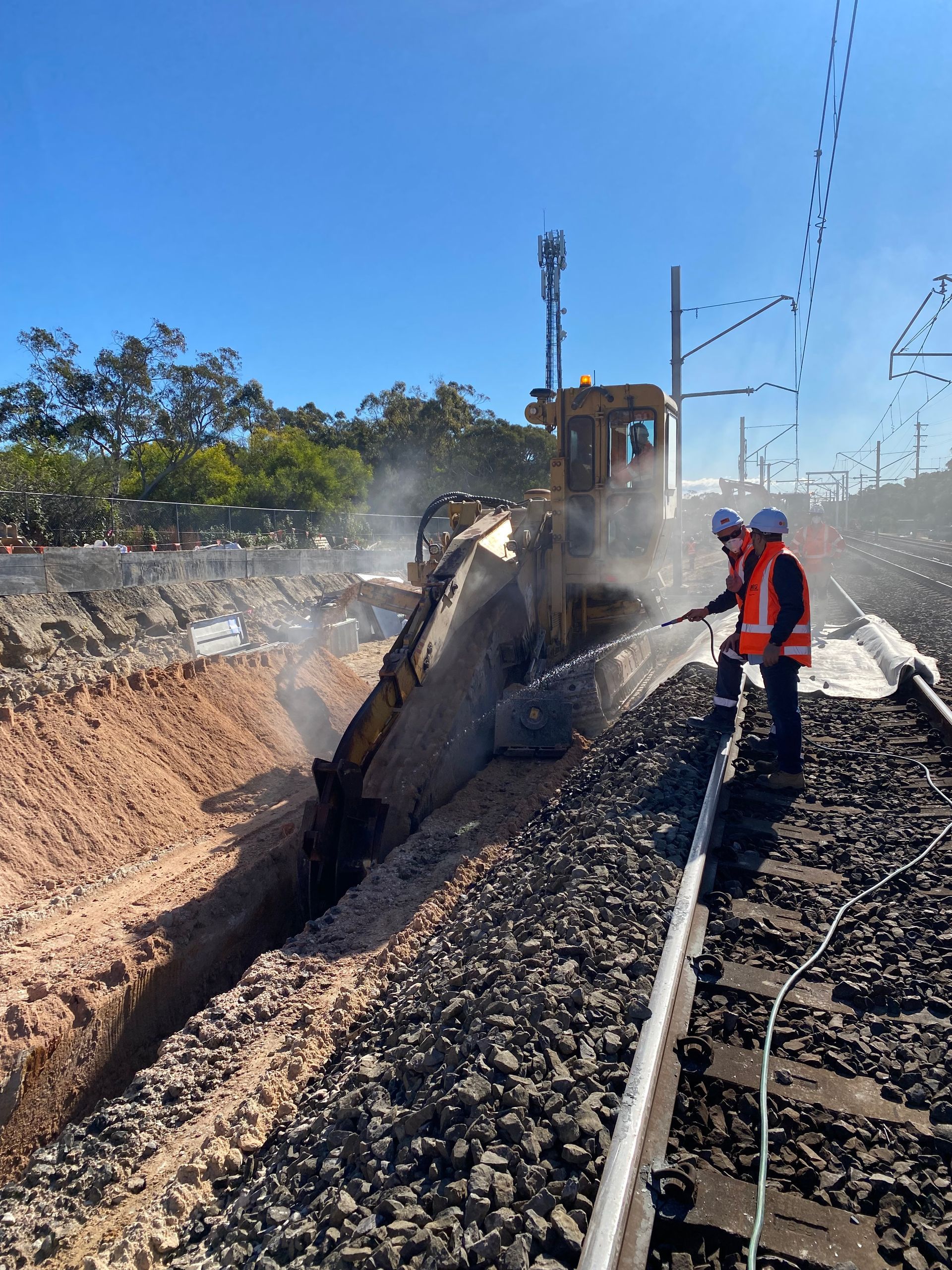 Two construction workers are standing next to a bulldozer on train tracks.