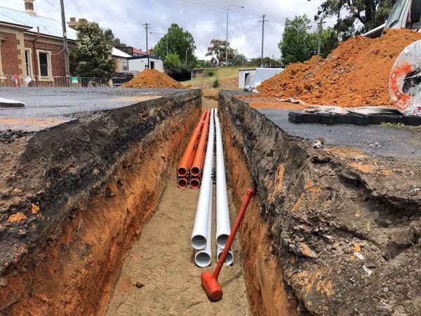 A bunch of pipes are laying in the dirt in a trench.