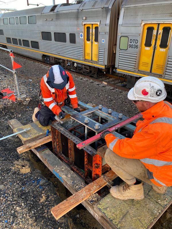 Two men are working on a railroad track next to a train.