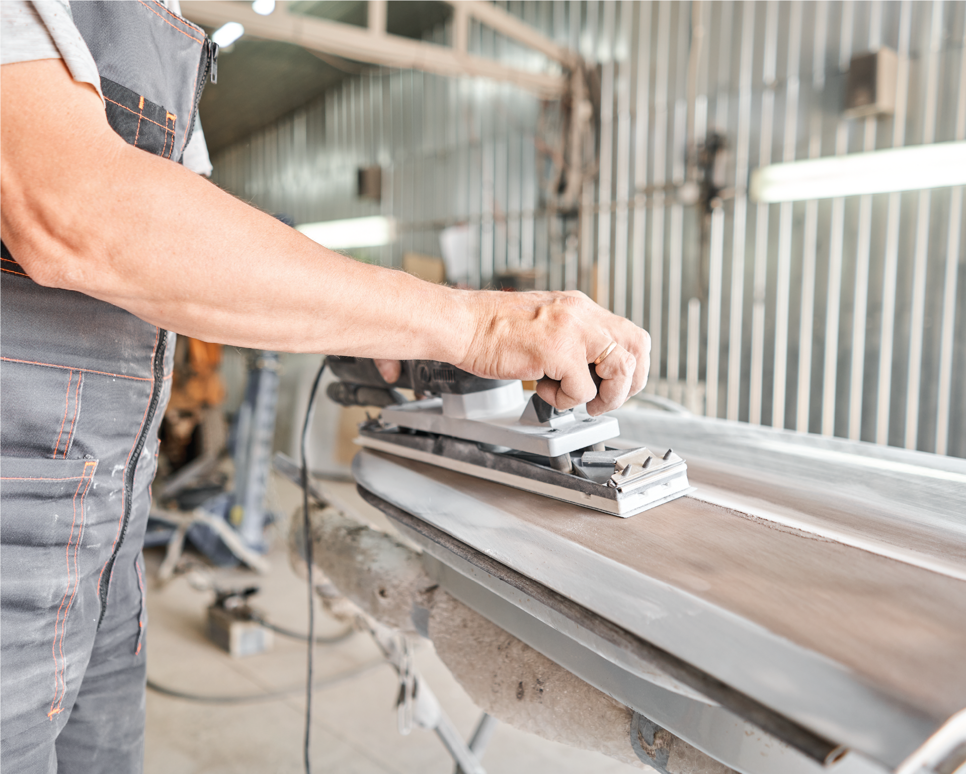 A man is sanding a piece of metal with a sander.