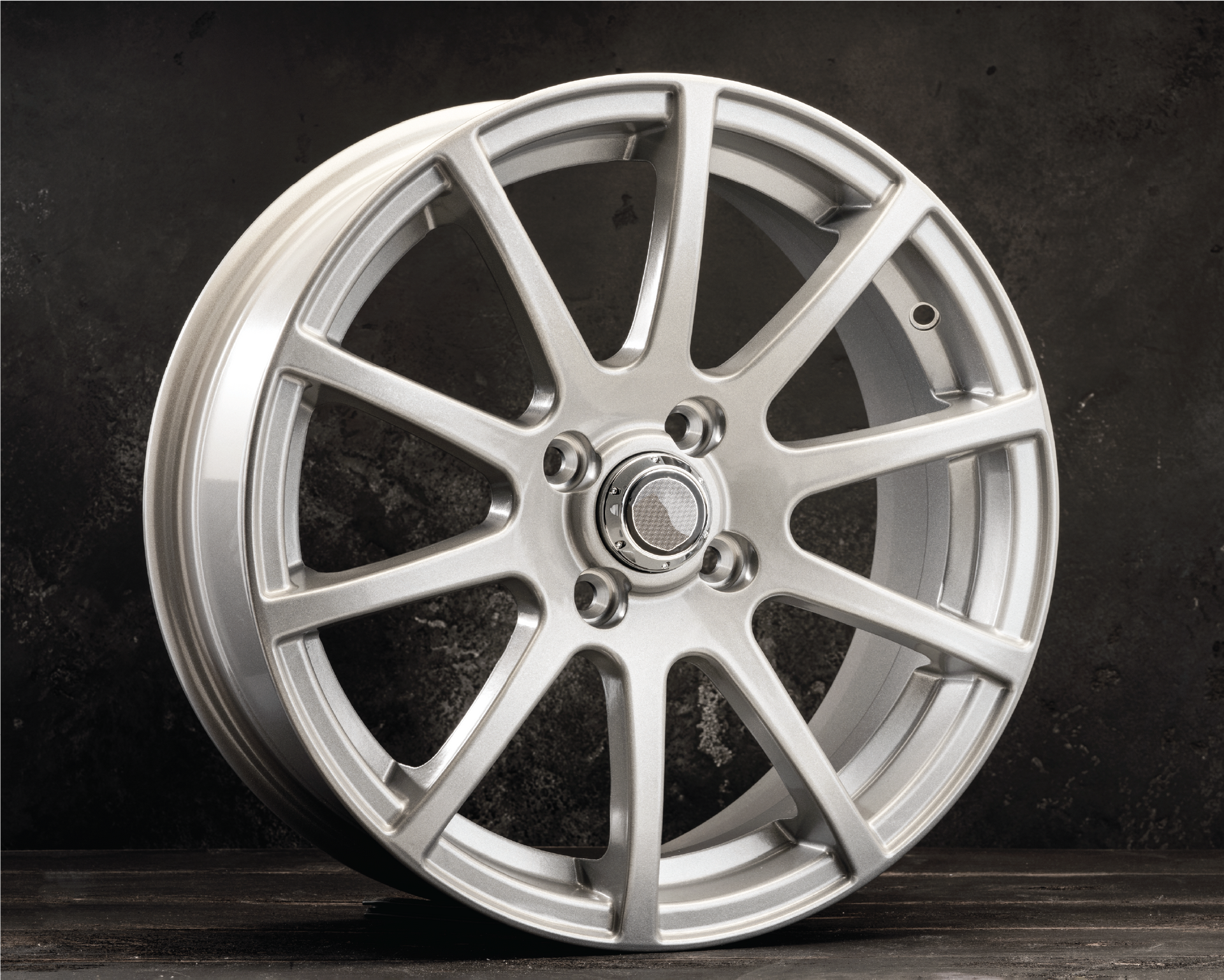 A silver car wheel is sitting on a wooden table.