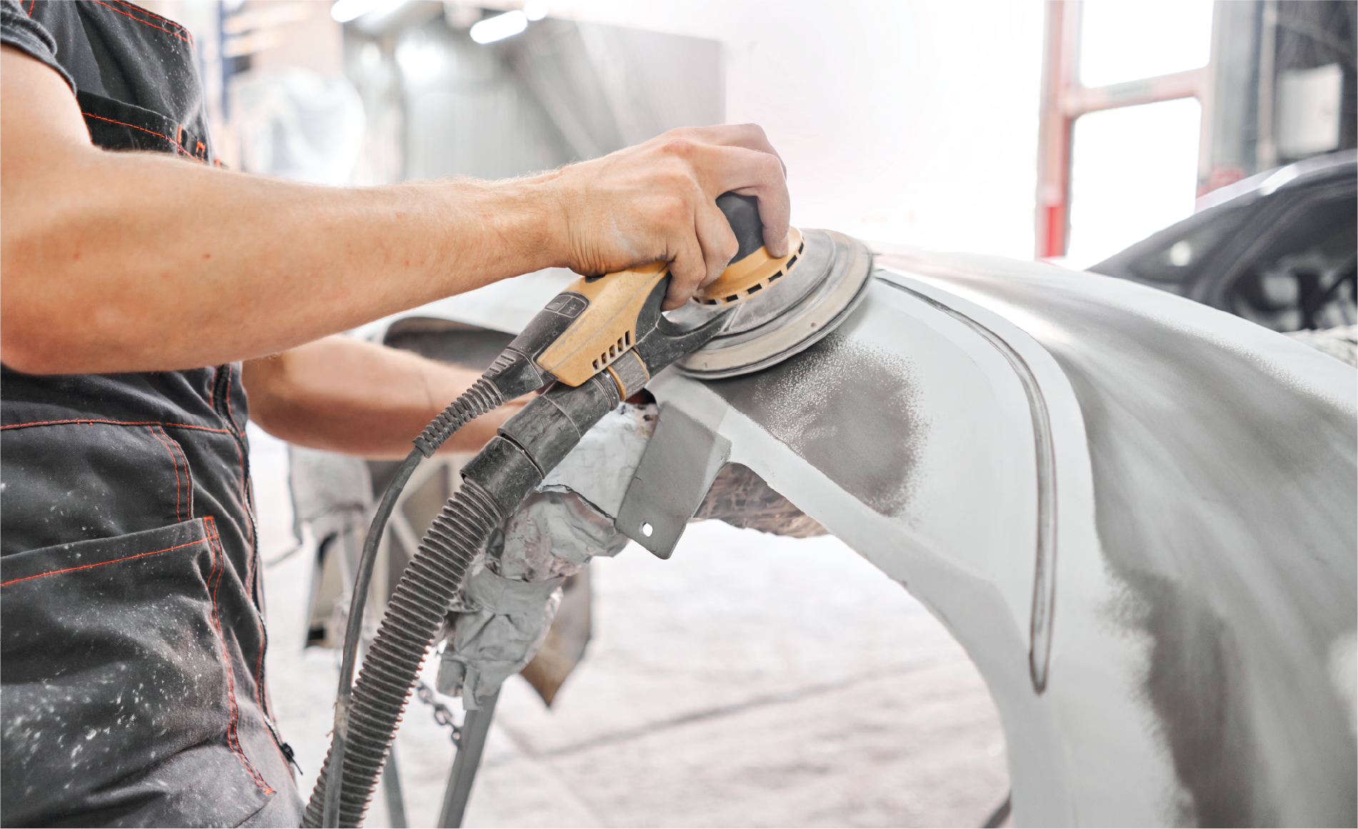 A man is sanding a car with a sander in a garage.