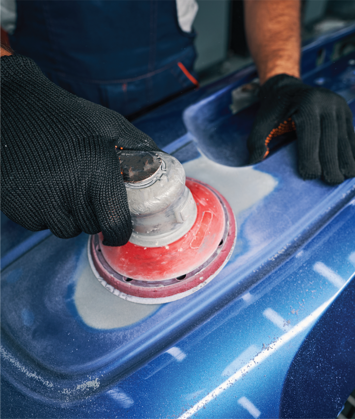 A man is polishing a blue car with a sander.