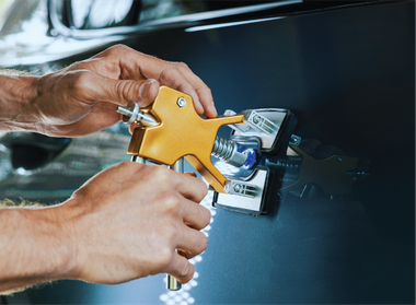 A person is using a tool to fix a dent on a car.