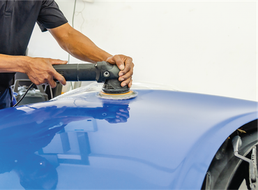 A man is polishing the hood of a blue car with a machine.