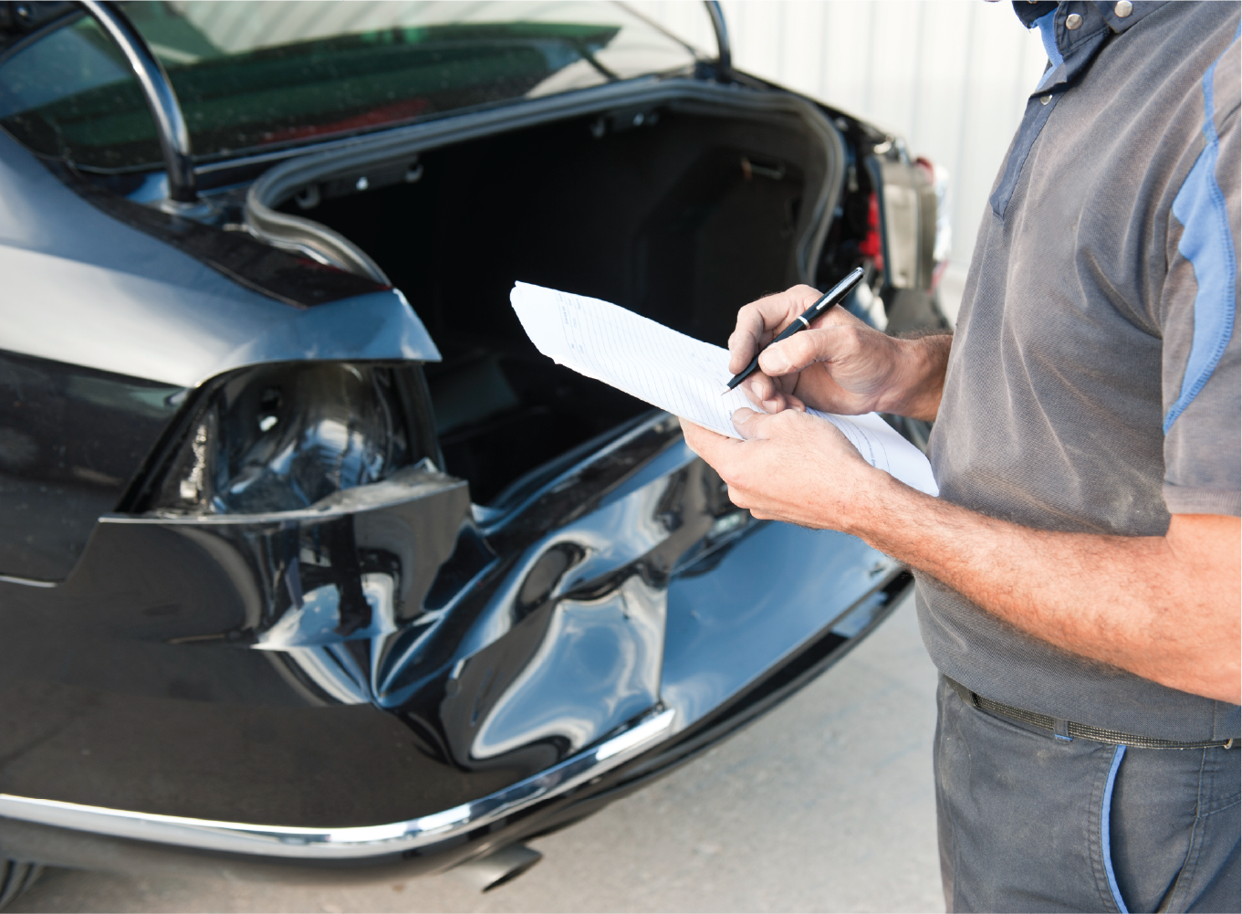 A man is writing on a piece of paper in front of a damaged car.