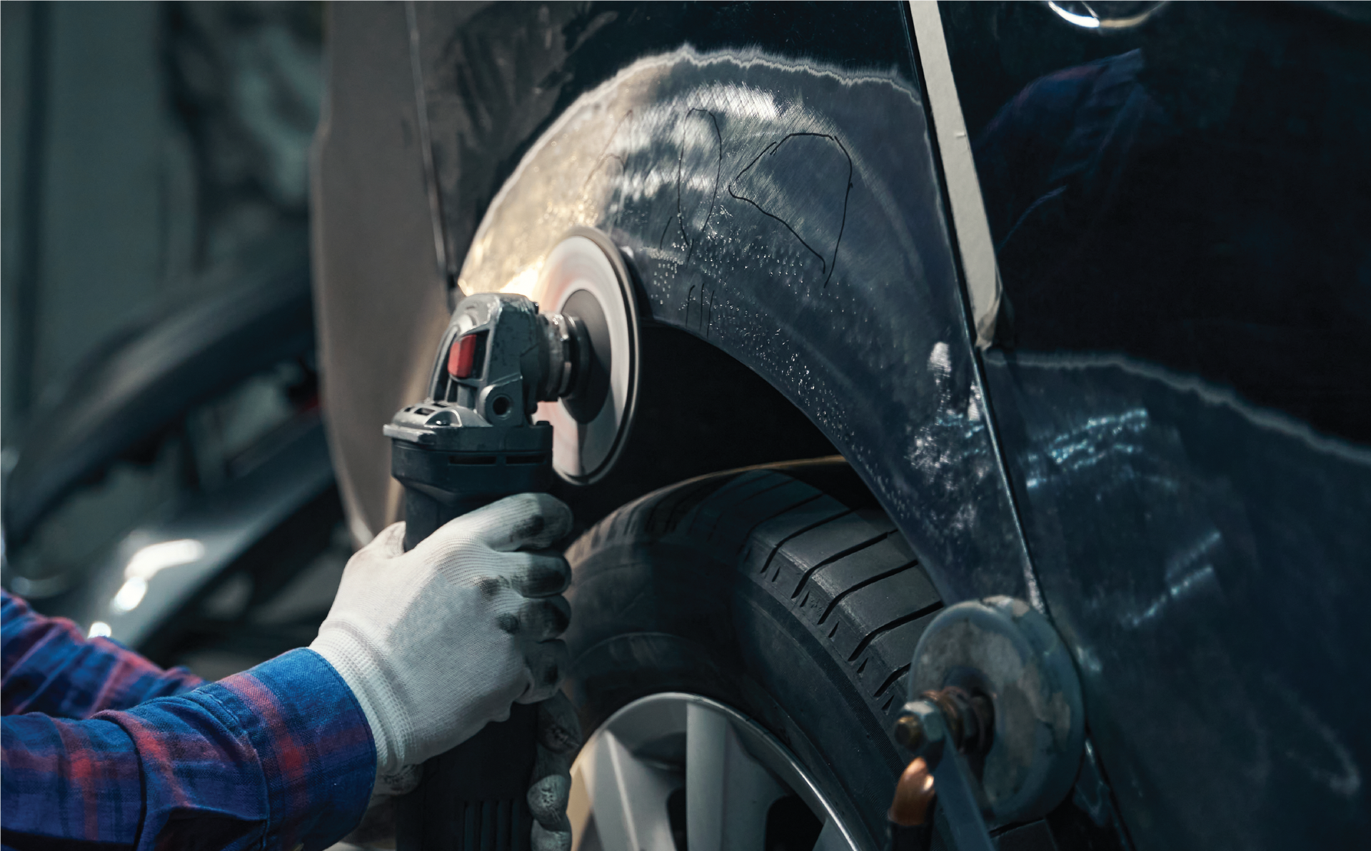 A man is polishing the fender of a car with a machine.