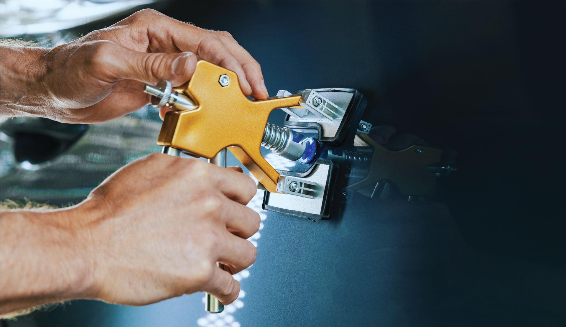 A person is holding a tool in their hands on a car hood.