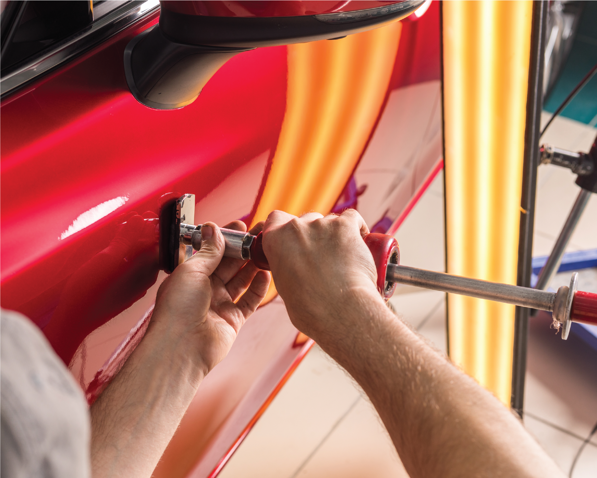 A man is working on a red car with a tool.