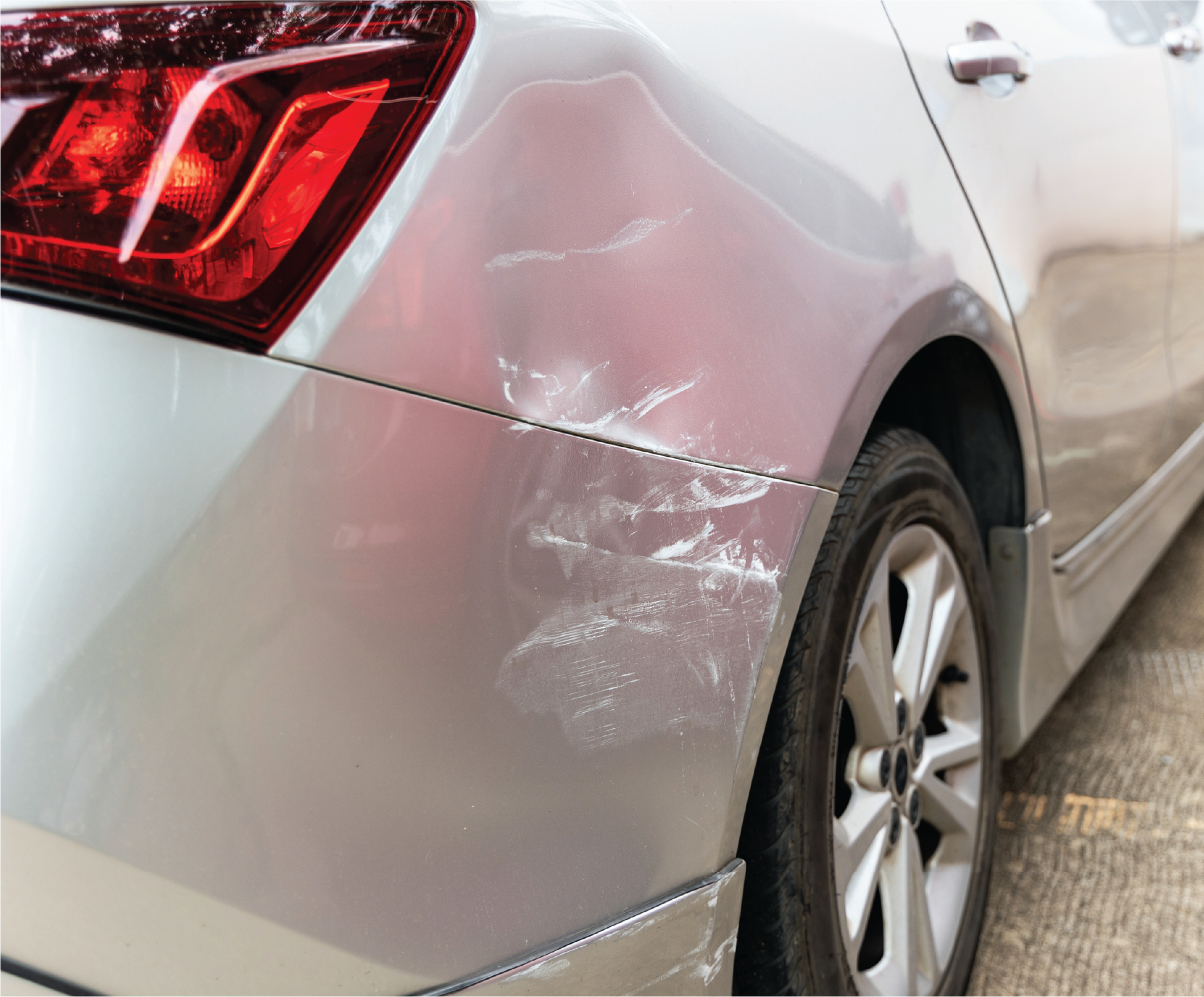 A silver car with a damaged bumper is parked on the side of the road.