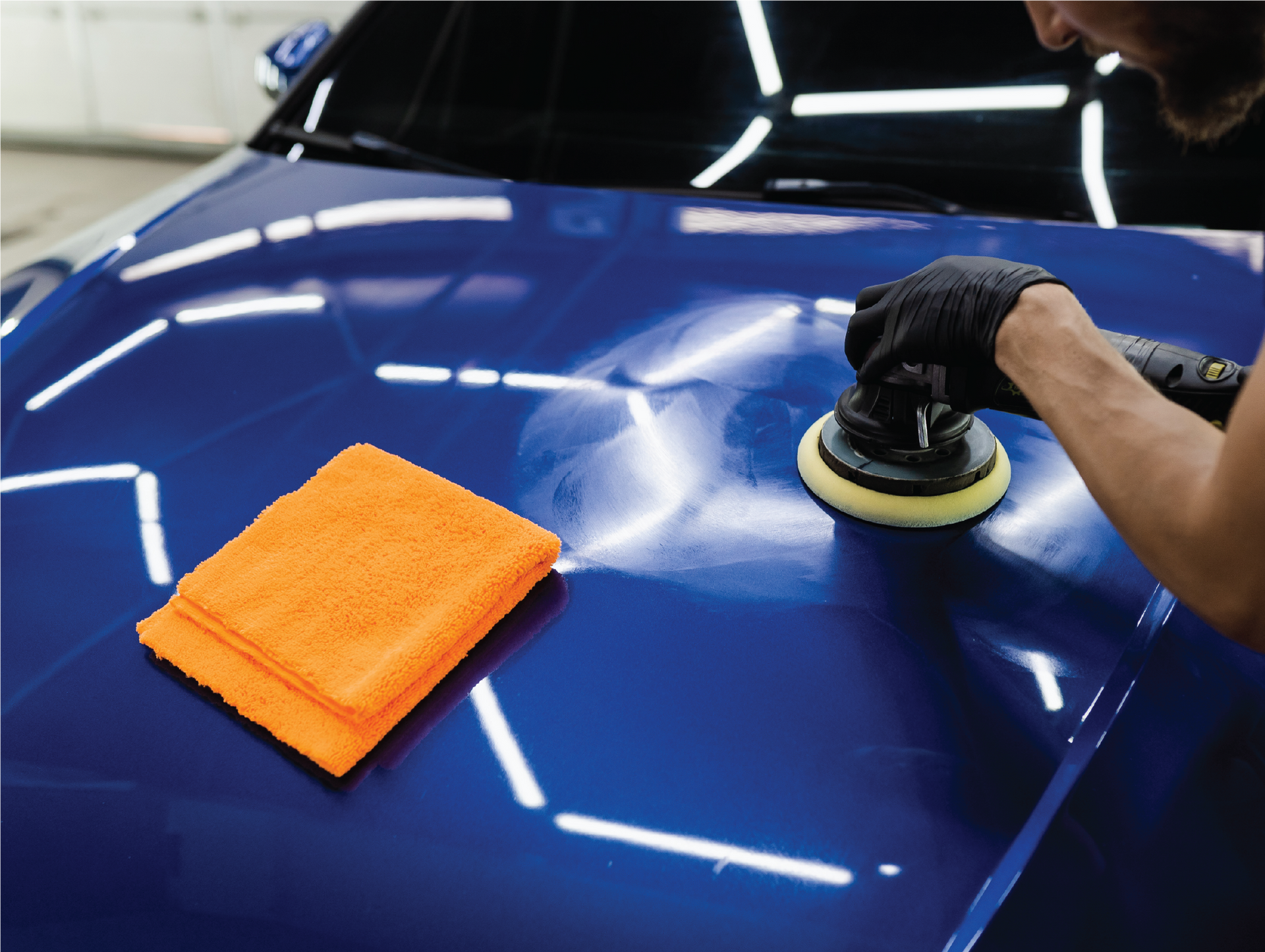 A man is polishing the hood of a blue car.