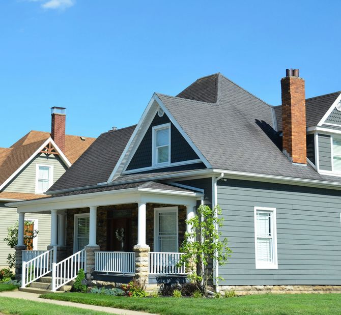 Gray house with white trim, front porch, and steep roof under a clear blue sky