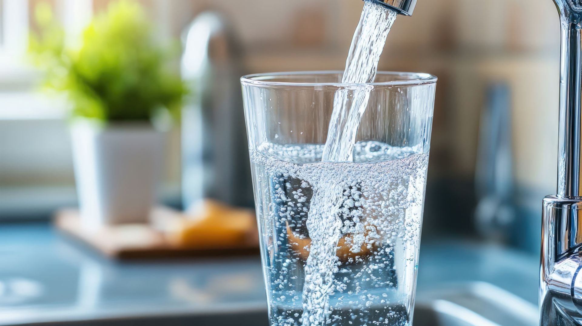 Clear water pouring from a kitchen faucet into a glass.