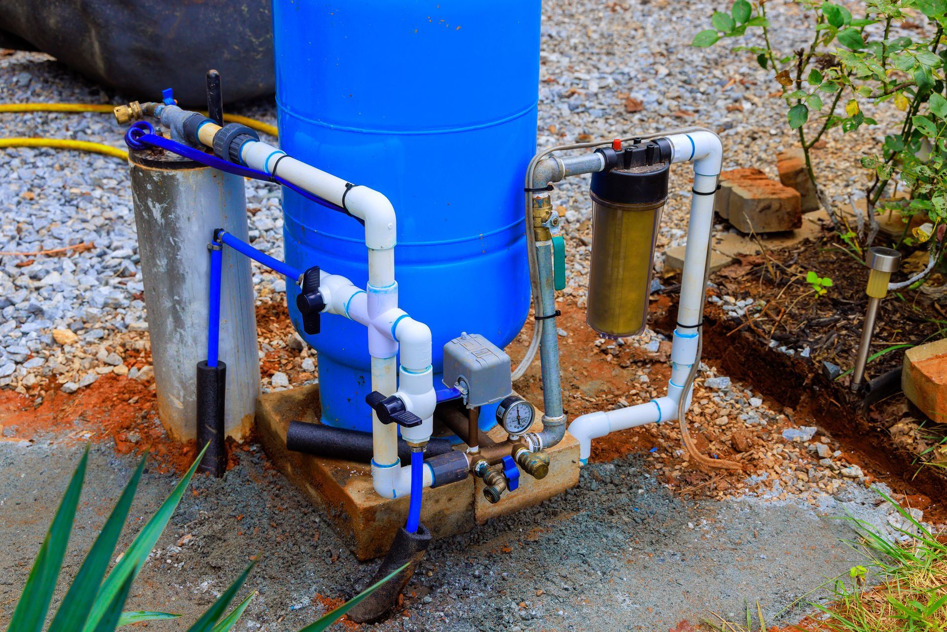 Blue water tank with white pipes, filter, and control box outdoors on a concrete base.