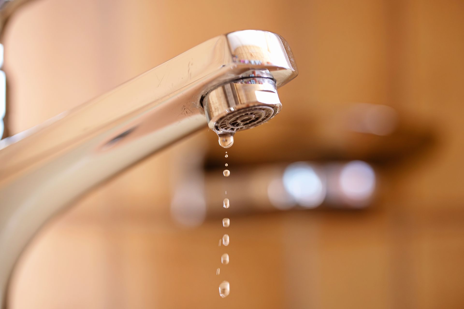 Chrome faucet dripping water over a sink, with a blurred bathroom background