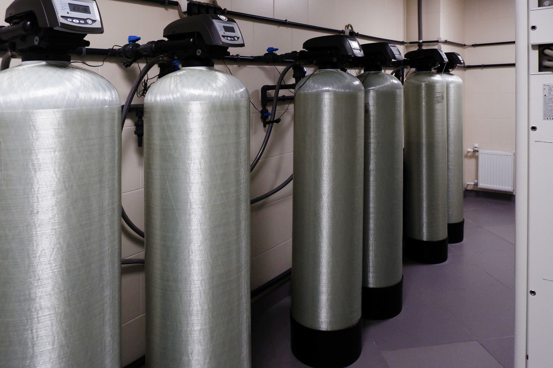 A row of industrial water filtration tanks with digital control heads installed in a mechanical utility room.