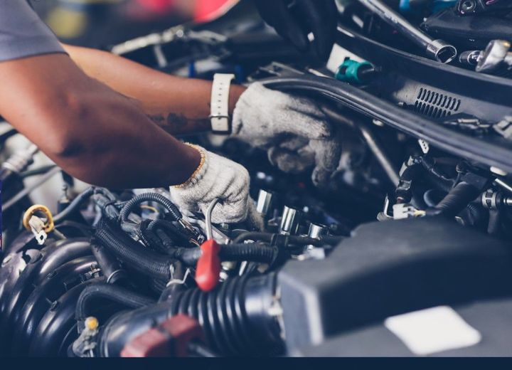 Mechanic working under a car hood with gloved hands and tools in a garage