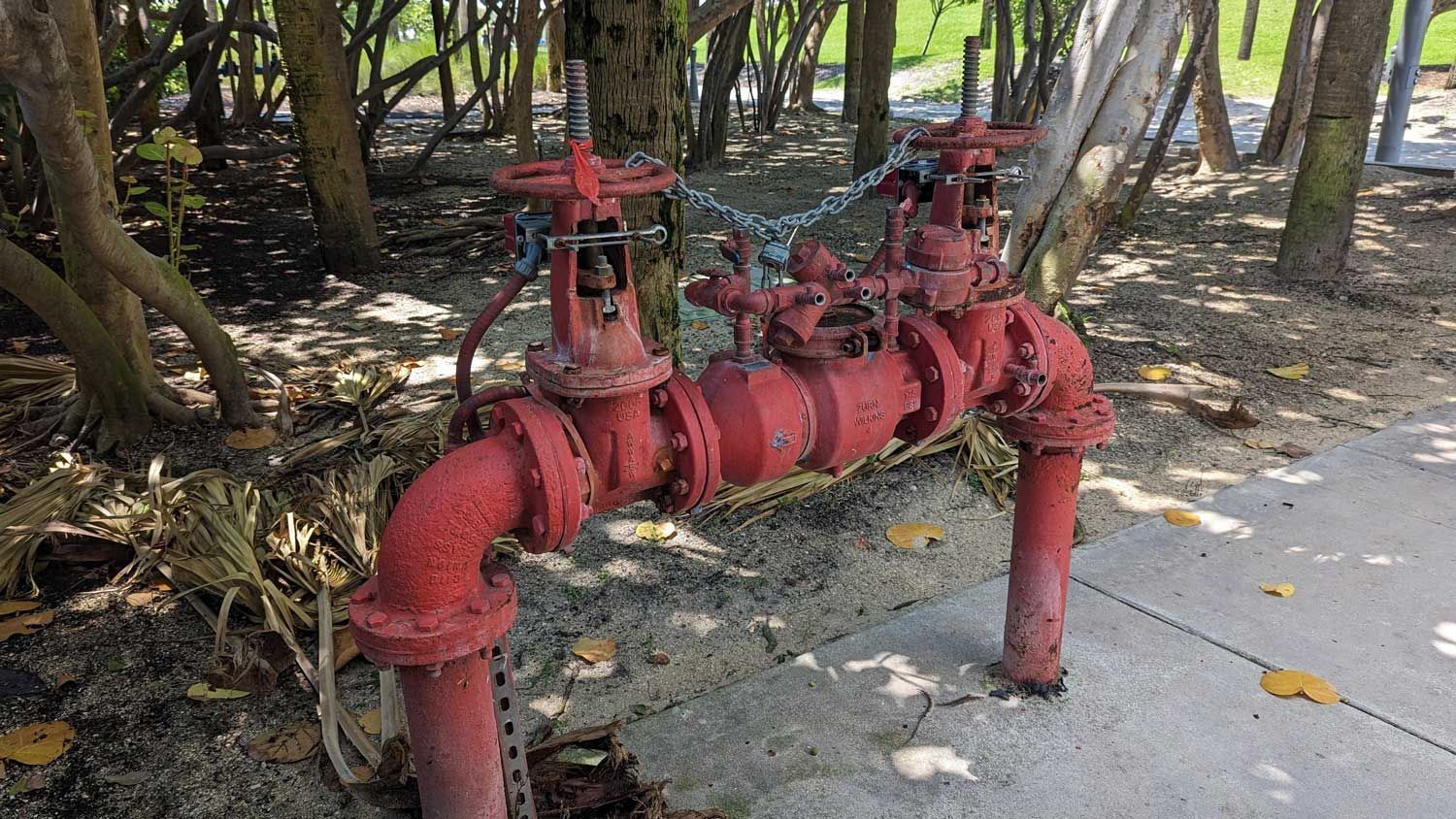 Red outdoor fire protection valves and pipes installed near trees beside a sidewalk path.