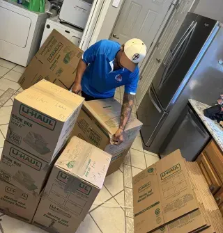 A man is standing in a kitchen surrounded by u-haul boxes.