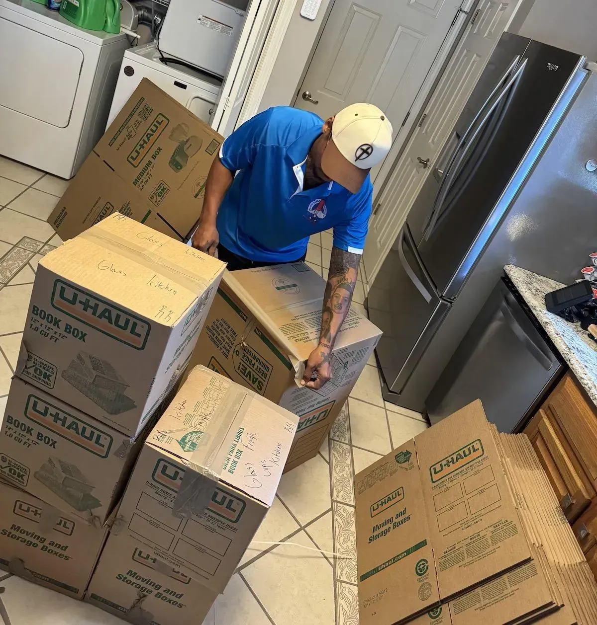 Man in blue shirt packing U-Haul boxes in kitchen with appliances, preparing for a move.