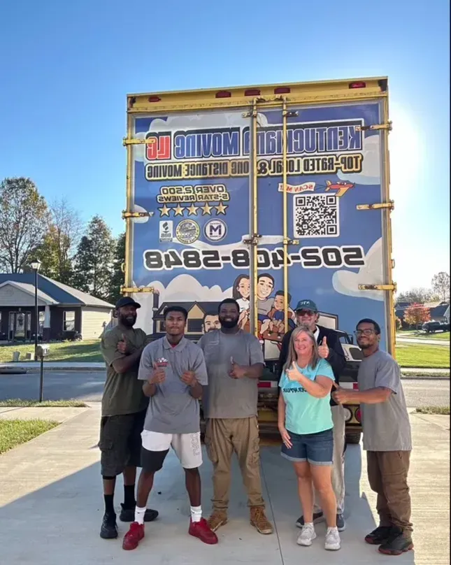 A group of movers and a customer pose with a moving truck, thumbs up.