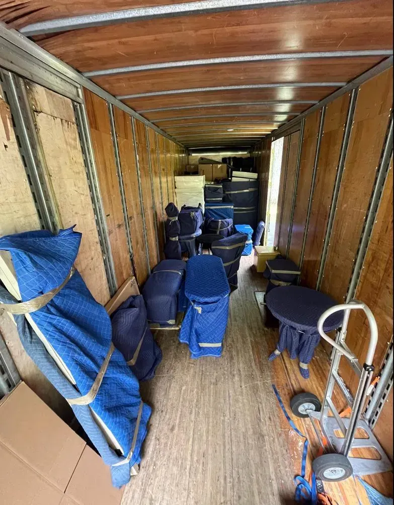Inside of a moving truck, filled with furniture wrapped in blue blankets and boxes.