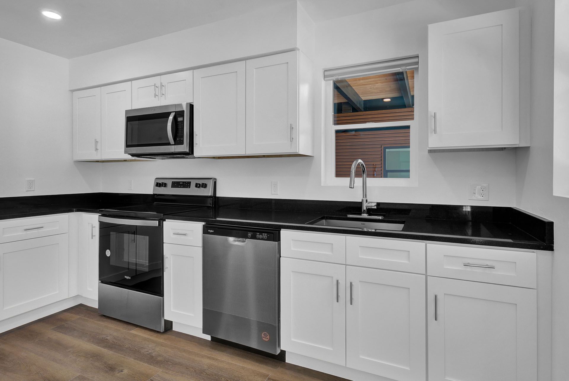 A kitchen with white cabinets , black counter tops , stainless steel appliances and a window.