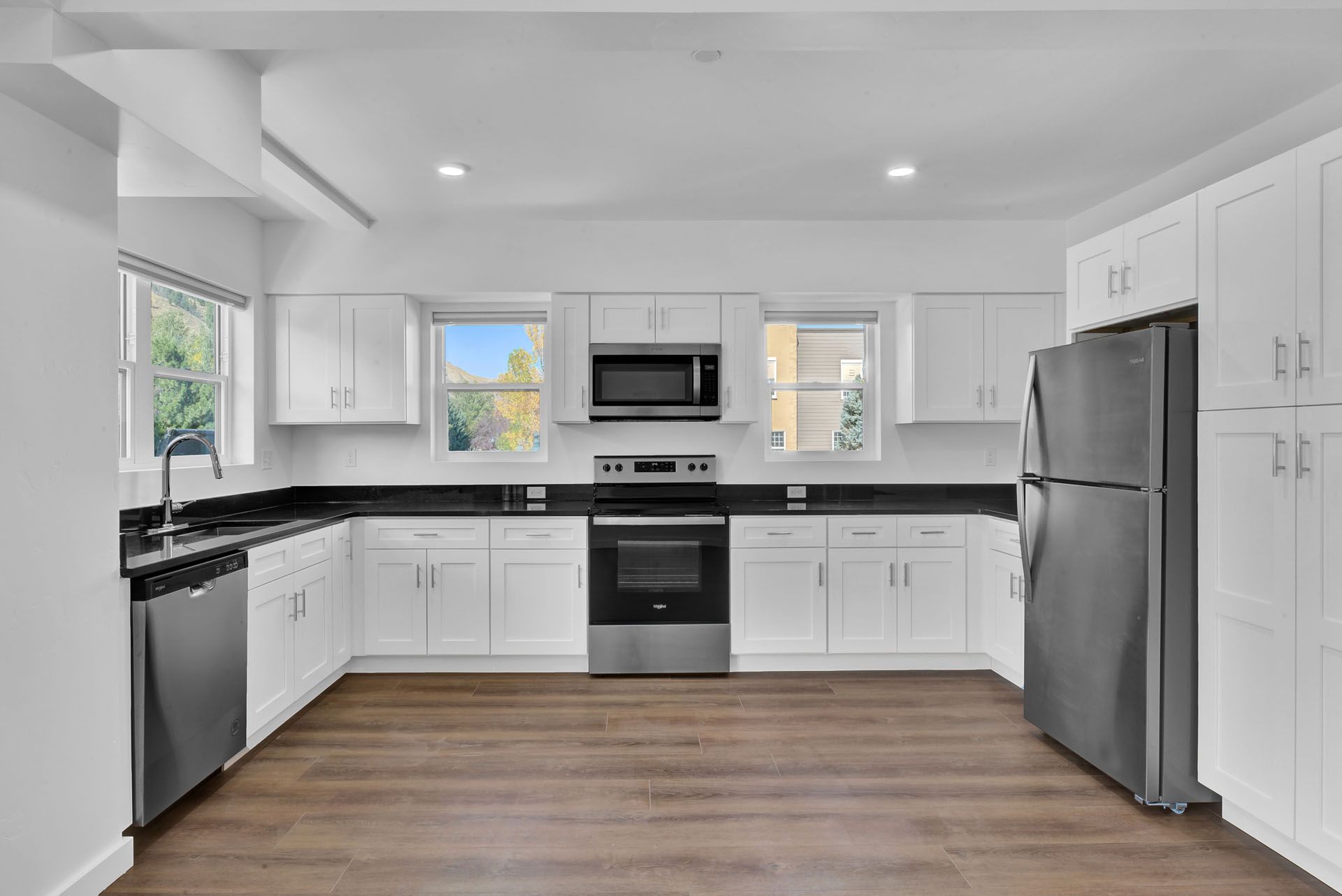 A kitchen with white cabinets , stainless steel appliances , a refrigerator and a microwave.