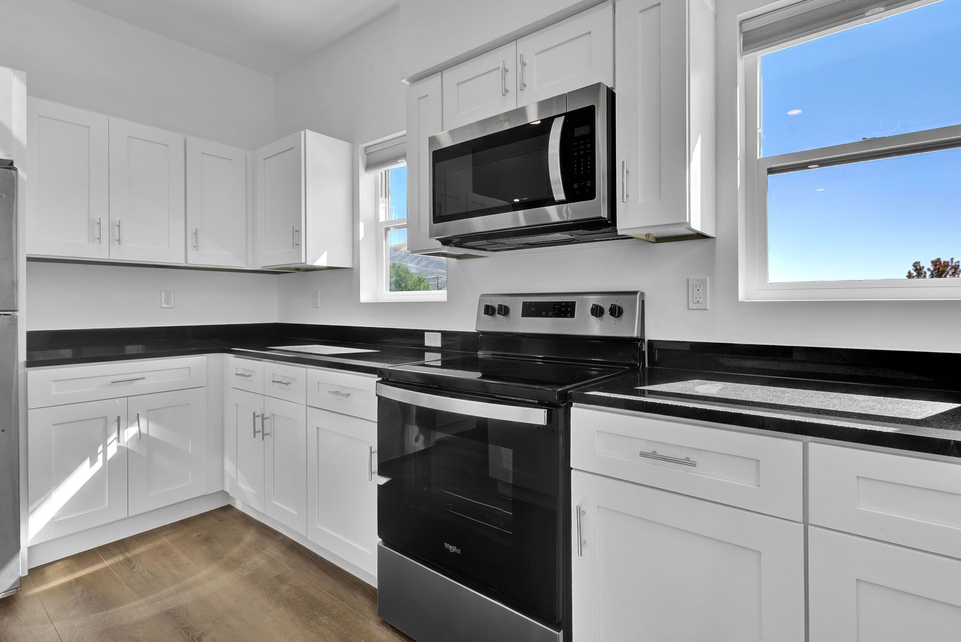 A kitchen with white cabinets , black counter tops , a stove , microwave and refrigerator.