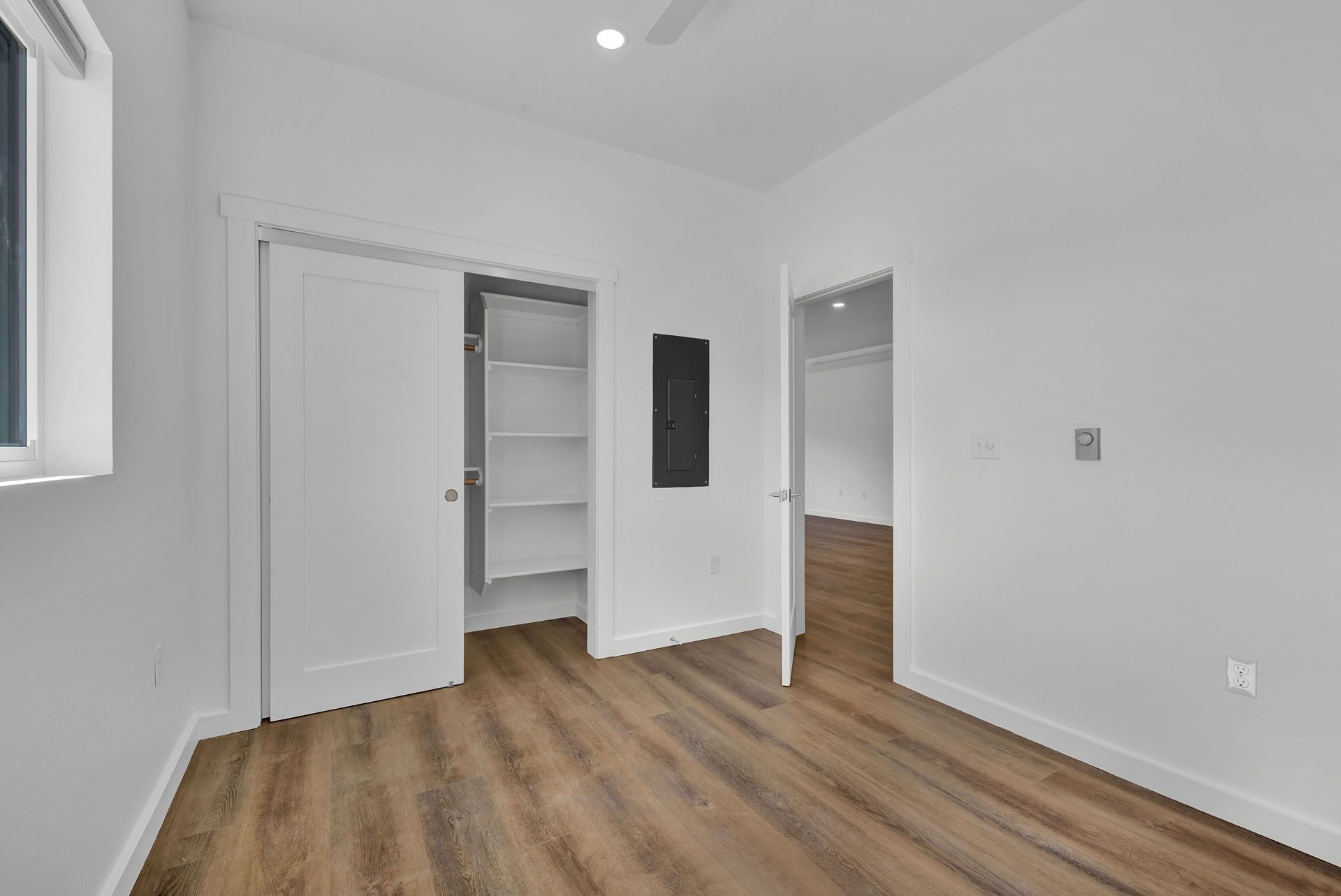 A bedroom with hardwood floors , white walls , and a closet.