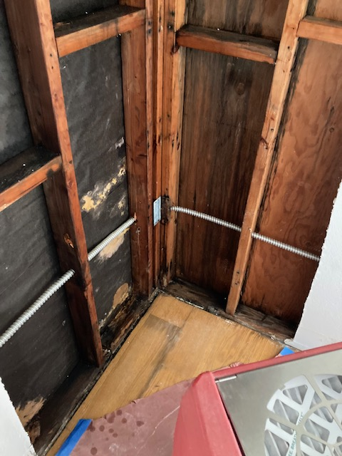 Interior corner of a room with exposed wooden studs, plywood, electrical wiring, and visible water damage.