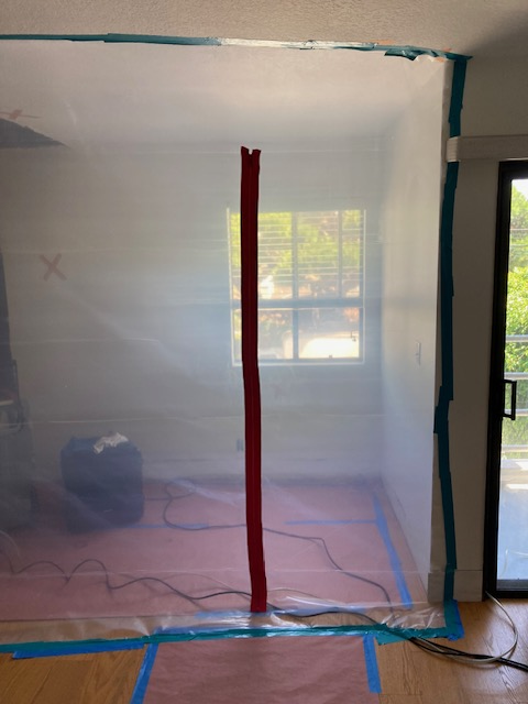 Room encased in plastic sheeting for containment. Red tape down the center. Blue tape along edges.