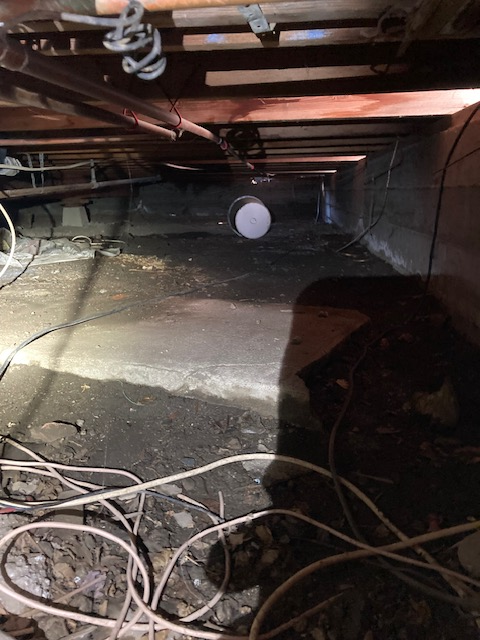 Crawl space under a house with dirt floor, wooden beams, and electrical wiring. White light illuminates the space.