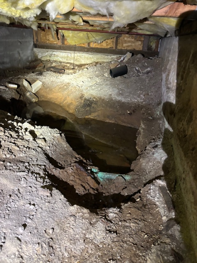 View from crawlspace, with exposed beams and dirt floor, and a black pipe.