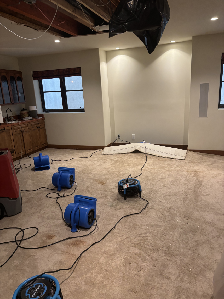 A room with water damage being dried; fans and equipment on the floor, exposed ceiling.