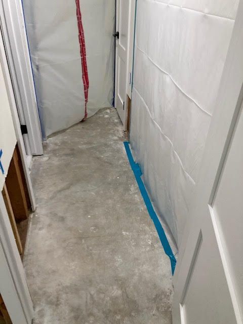 Concrete floor hallway, white walls and trim, with plastic sheeting and blue tape.