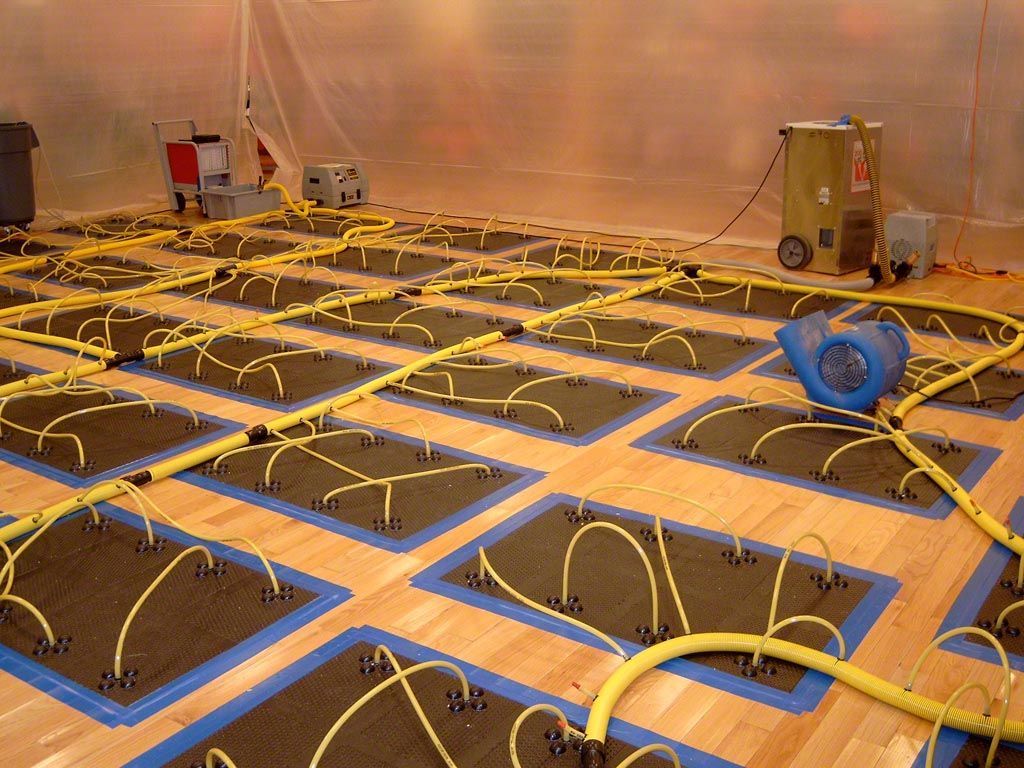 Flood remediation: floor covered with connected drying mats and equipment in a plastic-sheathed room.