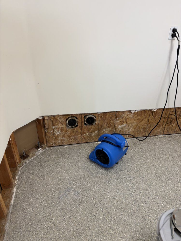 Blue blower on a damp, exposed wall corner. Two vents and a power cord are visible.